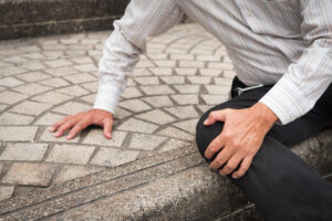 Slip and fall injury with man holding knee on uneven pavement